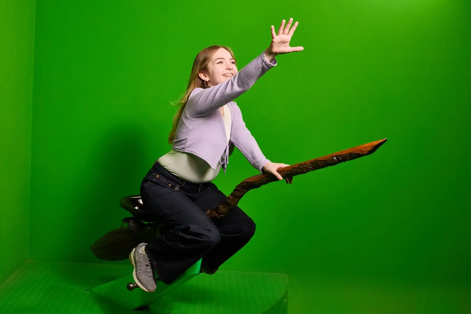A visitor sat on a broomstick in front of a green screen for the flying broomstick photo opportunity at Warner Bros. Studio Tour London.